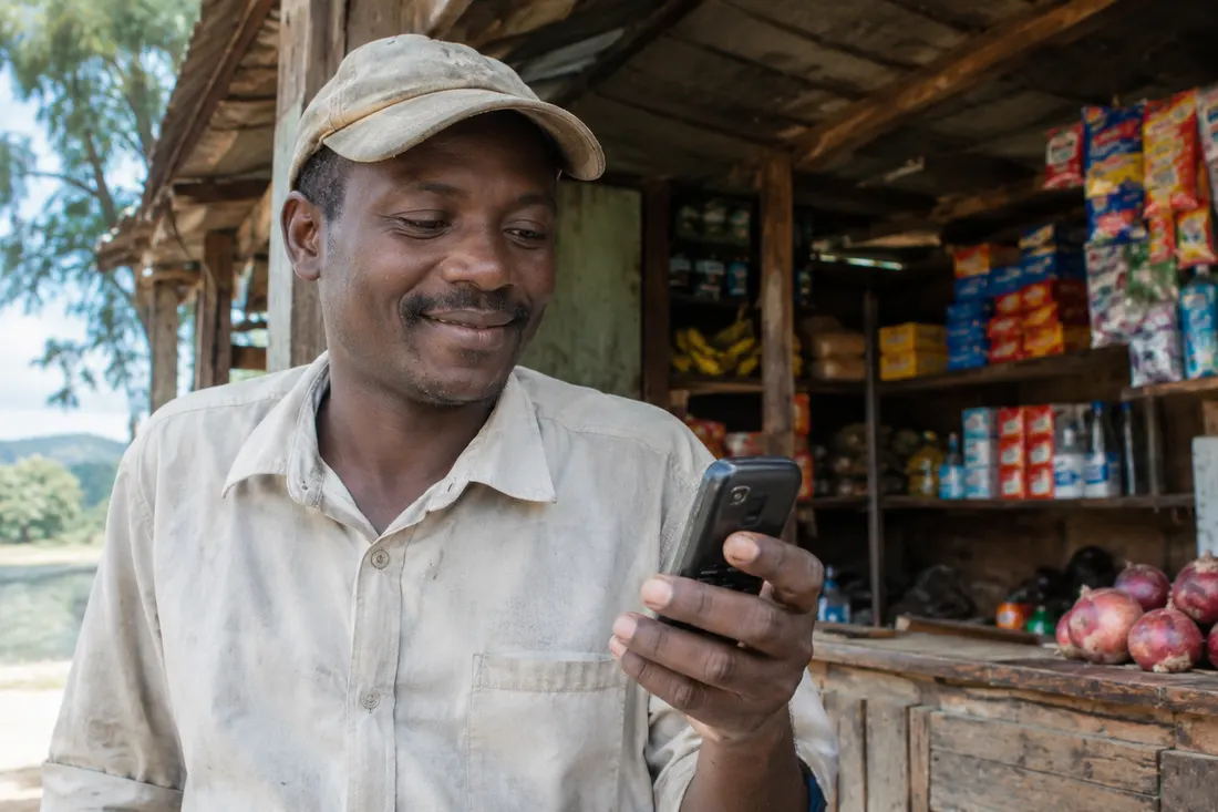 Illustration of a shopkeeper at a village stall, smiling as he reads a message on a basic mobile phone